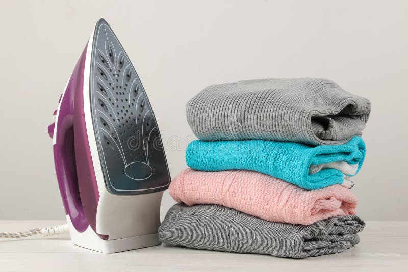 Iron and a Stack of Colored Clothes on a White Background. Ironing of