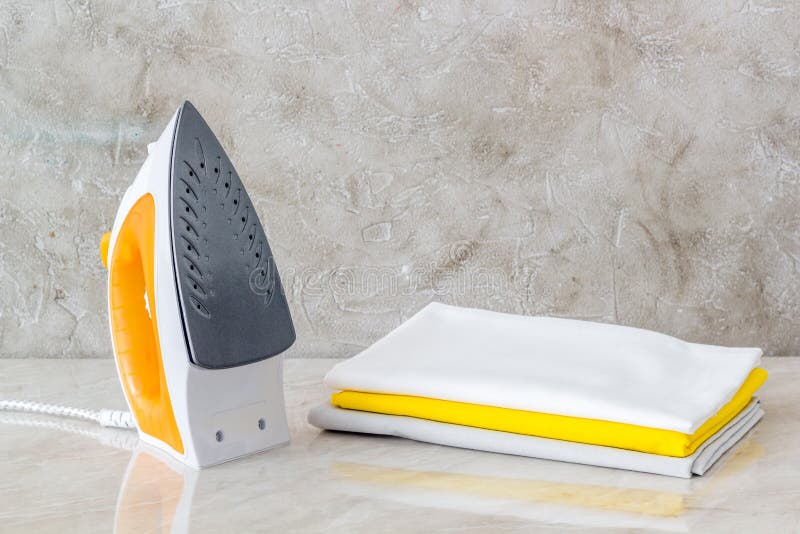 Iron and a Stack of Colored Clothes on a White Background. Ironing of