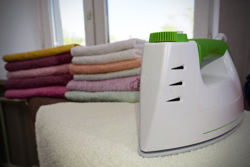 Ironing linen with steam generator. A stack of ironed towels lying next to the iron. Teflon sole plate covered with small holes.