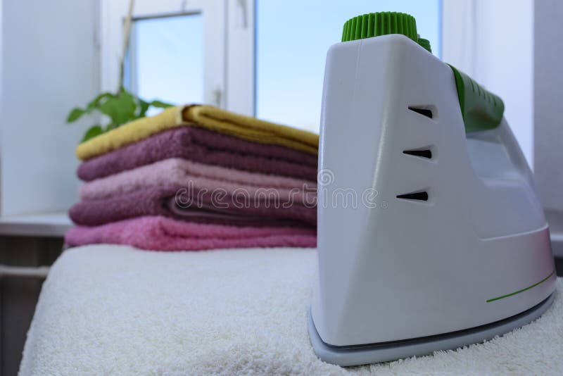 Ironing linen with steam generator. A stack of ironed towels lying next to the iron. Teflon sole plate covered with small holes. Clean, heat.