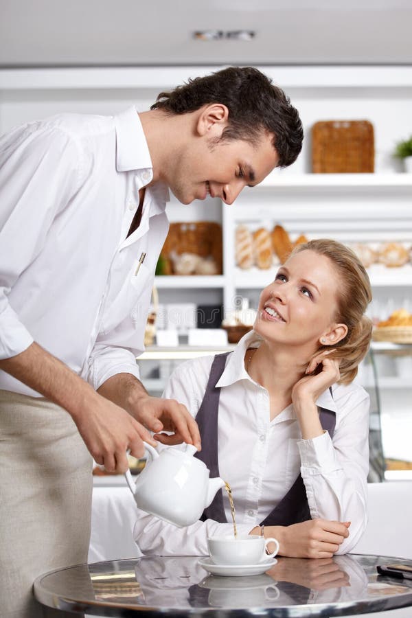 Joven mesero vierte té sobre el el cliente en cafetería.