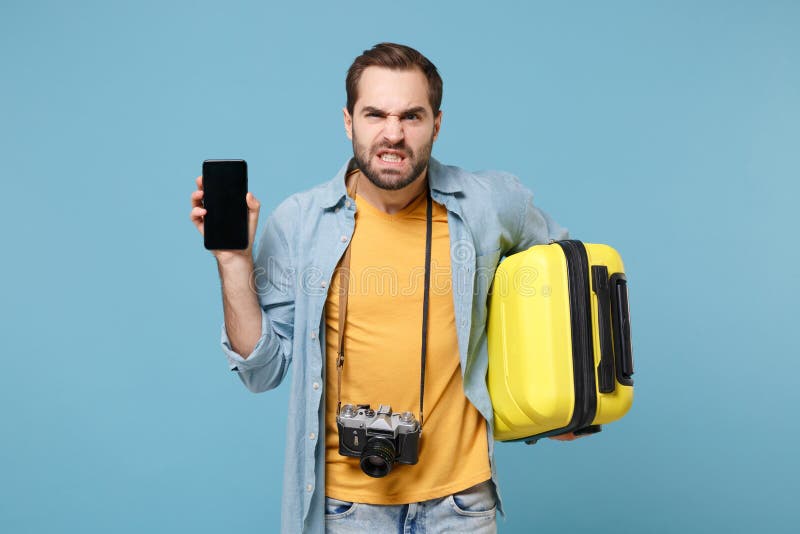 Irritated traveler tourist man in casual clothes with photo camera isolated on blue background. Passenger traveling abroad on weekends. Air flight journey Hold suitcase mobile phone with blank screen. Irritated traveler tourist man in casual clothes with photo camera isolated on blue background. Passenger traveling abroad on weekends. Air flight journey Hold suitcase mobile phone with blank screen