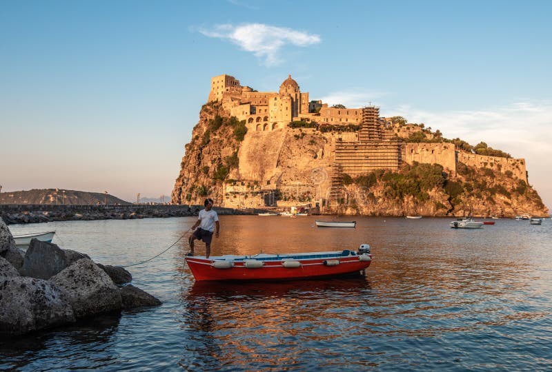 Ischia, Italy June 20, 2017: Boatman with a boat on the background of the Aragonese castle royalty free stock photography Ischia, Italy June 20, 2017: Boatman with a boat on the background of the Aragonese castle royalty free stock photography