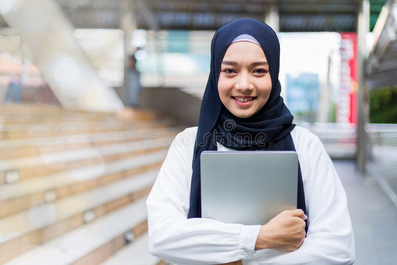 Islamska studentka lub pracująca kobieta stojąca ze skrzyżowanymi ramionami, trzymająca laptopa uśmiechniętego z ufnością zdjęcie royalty free