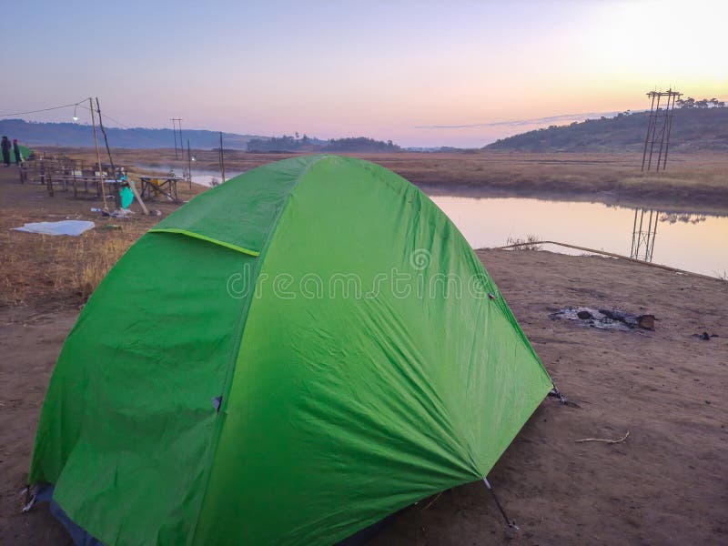 Isolated camping tent at calm lake shore with dramatic sunrise colorful sky reflection at morning in details