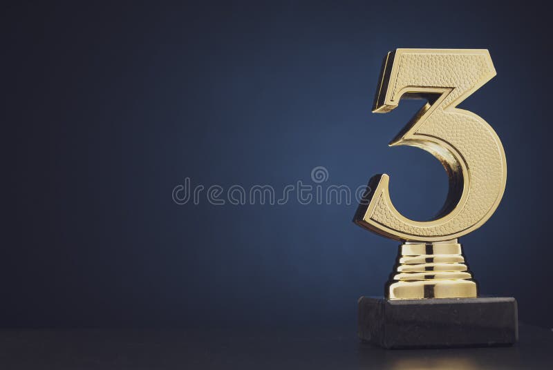 Sharp close up on single isolated gold colored plastic statue of number 3 over blue and black background. Sharp close up on single isolated gold colored plastic statue of number 3 over blue and black background