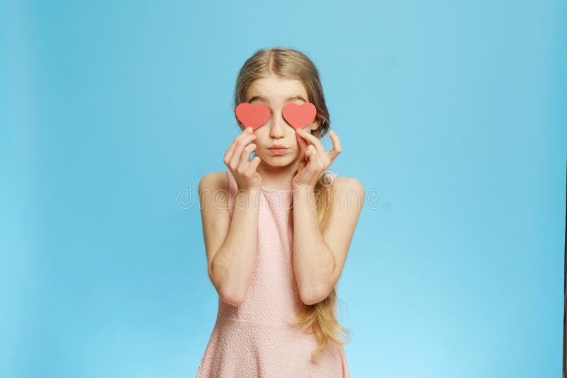 Little girl and paper hearts. Isolated little girl covers her eyes with paper hearts on a blue background.