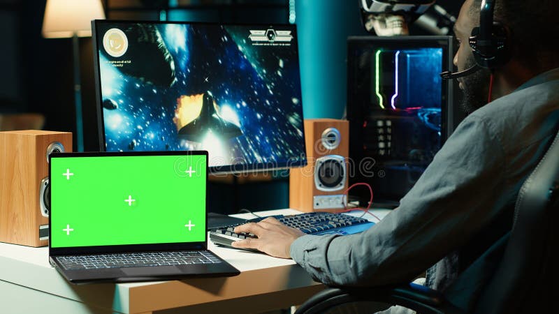 Isolated screen laptop next to streamer competing in online game. Isolated screen laptop next to professional streamer competing in online multiplayer videogame, streaming live at home. Mockup notebook and man playing on PC, using headphones to talk with audience