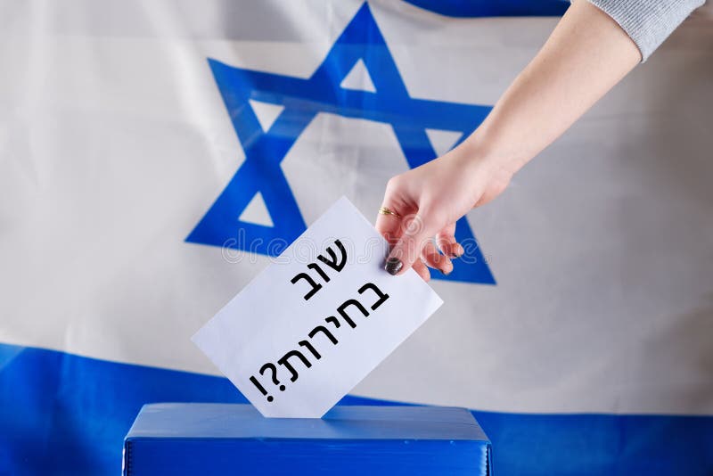 Israeli woman votes at a polling station on election day. Close up of hand. Hebrew text elections again.