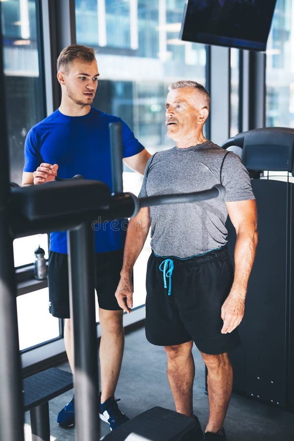Istruttore personale che dà istruzioni all'uomo più anziano alla palestra immagini stock libere da diritti Istruttore personale che dà istruzioni all'uomo più anziano alla palestra immagini stock libere da diritti
