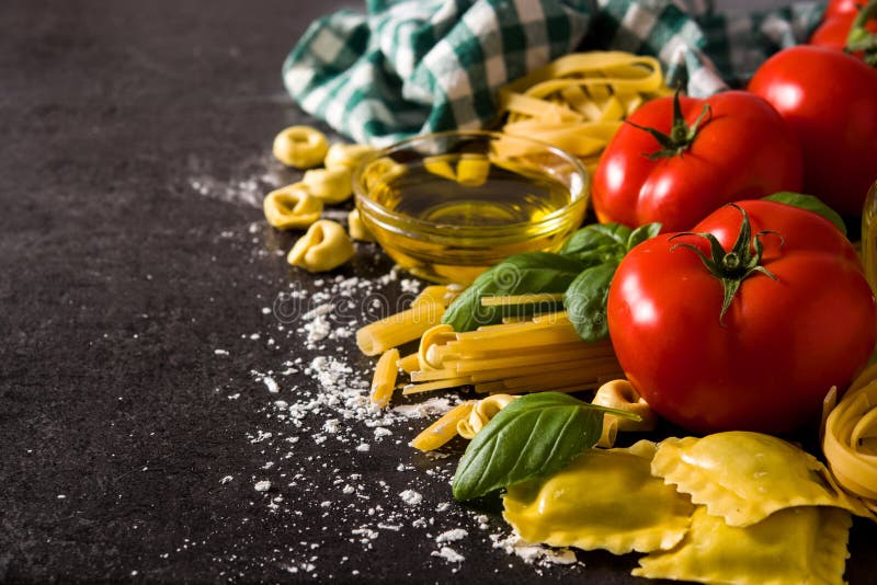 Italian pasta and ingredients. Ravioli, penne pasta, spaghetti, tortellini, tomatoes and basil on black background. copy space. Italian pasta and ingredients. Ravioli, penne pasta, spaghetti, tortellini, tomatoes and basil on black background. copy space