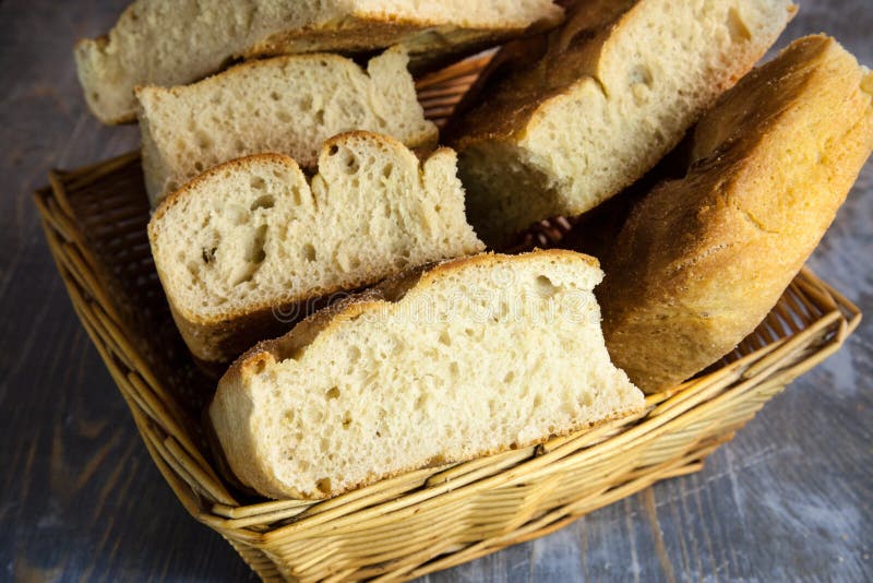 Italian bread of Focaccia Genovese type on display on a basket on a rustic wooden table, sliced in several squared pieces. royalty free stock photography