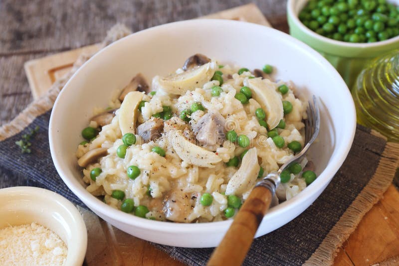 Italian cuisine. Plate of mushroom risotto with green pea, artichokes and grated parmesan cheese  on wooden background