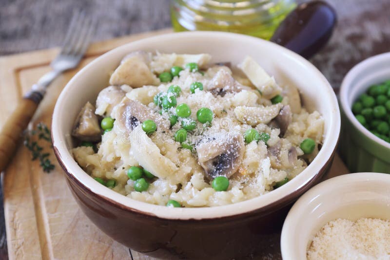 Italian cuisine. Plate of mushroom risotto with green pea, artichokes and grated parmesan cheese on wooden background