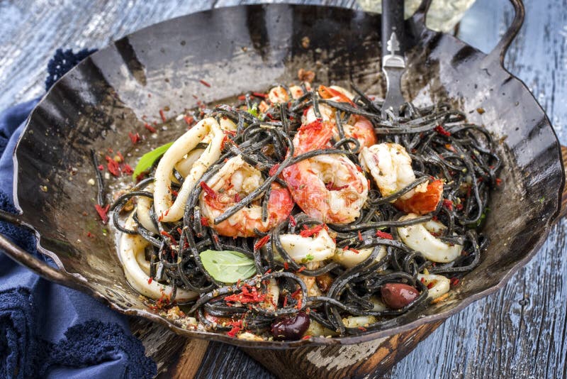 Italian linguine con tinta de calamari and prawns with olives in a rustic wrouth iron pan