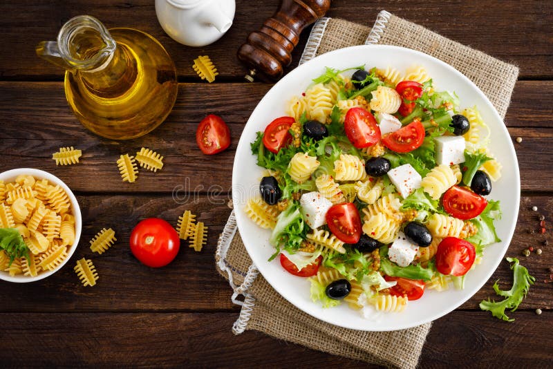 Italian pasta salad with fresh tomato, cheese, lettuce and olives on wooden background. Mediterranean cuisine. Cooking lunch. Hea royalty free stock photos Italian pasta salad with fresh tomato, cheese, lettuce and olives on wooden background. Mediterranean cuisine. Cooking lunch. Hea royalty free stock photos