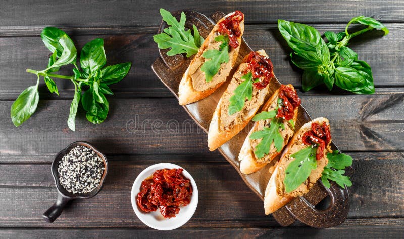 Italian sandwiches - bruschetta with meat pate, arugula, sun dried tomato and seeds on ciabatta bread. On dark wooden table. Delicious snacks, sandwiches stock photo Italian sandwiches - bruschetta with meat pate, arugula, sun dried tomato and seeds on ciabatta bread. On dark wooden table. Delicious snacks, sandwiches stock photo