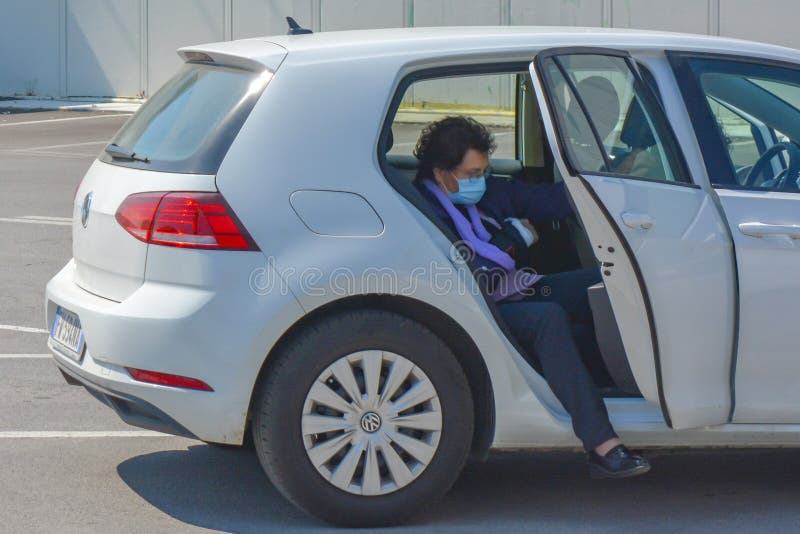 An italian woman open the car door, ready to get out. Lady wears face mask for covid19, rules after reopening in Europe. stock image An italian woman open the car door, ready to get out. Lady wears face mask for covid19, rules after reopening in Europe. stock image