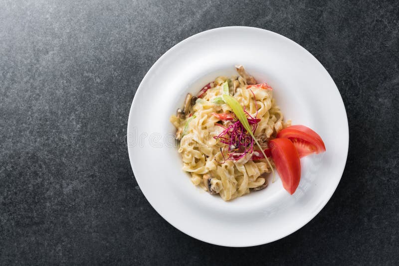 Italiensk deg av carbonariaen med champinjoner med kräm- sås på en vit platta arkivbild Italiensk deg av carbonariaen med champinjoner med kräm- sås på en vit platta arkivbild