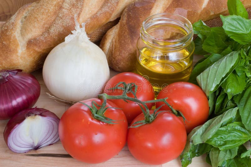 Common ingredients in italian cooking: tomatoes,basil,onions,olive oil, and fresh bread on a bread board. Common ingredients in italian cooking: tomatoes,basil,onions,olive oil, and fresh bread on a bread board