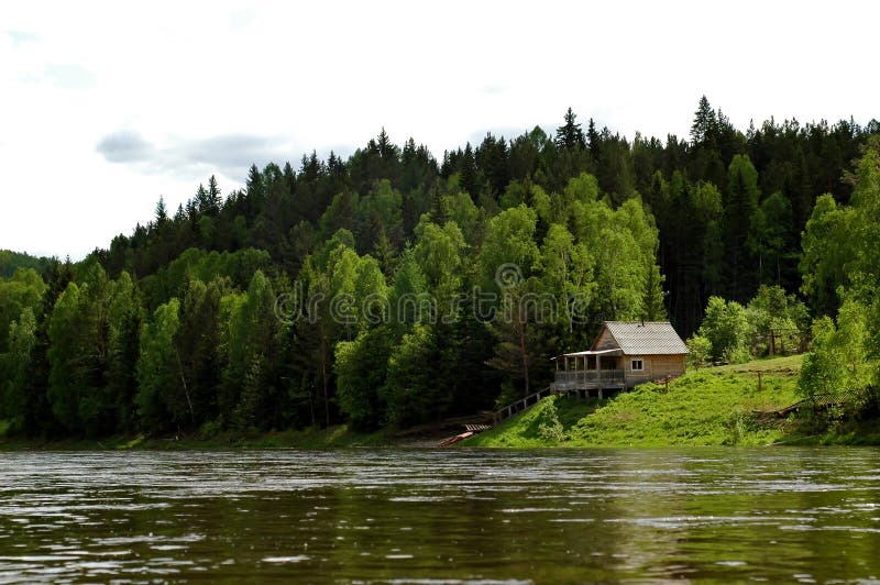 Magnificent landscape. The Siberian mountain river Mana against a mountain taiga and the sky. Izba on the bank. Magnificent landscape. The Siberian mountain river Mana against a mountain taiga and the sky. Izba on the bank.