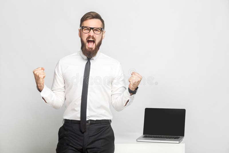 Ja! Het portret van knappe gelukkige gebaarde jonge zakenman in wit overhemd en de avondkleding bevinden zich in bureau zegeviere stock foto Ja! Het portret van knappe gelukkige gebaarde jonge zakenman in wit overhemd en de avondkleding bevinden zich in bureau zegeviere stock foto