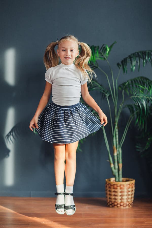 8 jaar oude Mooi verzamelde weinig blondemeisje zich met haar in staarten, witte t-shirt, witte sokken en grijze rok springend in royalty-vrije stock afbeelding 8 jaar oude Mooi verzamelde weinig blondemeisje zich met haar in staarten, witte t-shirt, witte sokken en grijze rok springend in royalty-vrije stock afbeelding