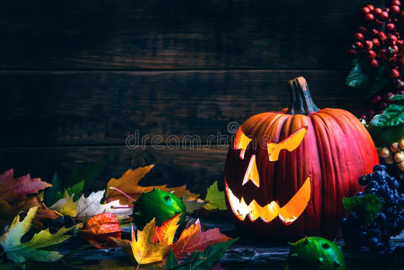 Jack o lanterne di zucca di Halloween viso su sfondo di legno e in autunno foglie.