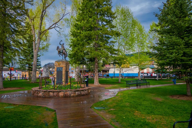 JACKSON HOLE WYOMING, USA - MAJ 23, 2018: Utomhus- sikt av turisten som nästan går i en parkera en bronsstaty av cowboyen arkivbild JACKSON HOLE WYOMING, USA - MAJ 23, 2018: Utomhus- sikt av turisten som nästan går i en parkera en bronsstaty av cowboyen arkivbild