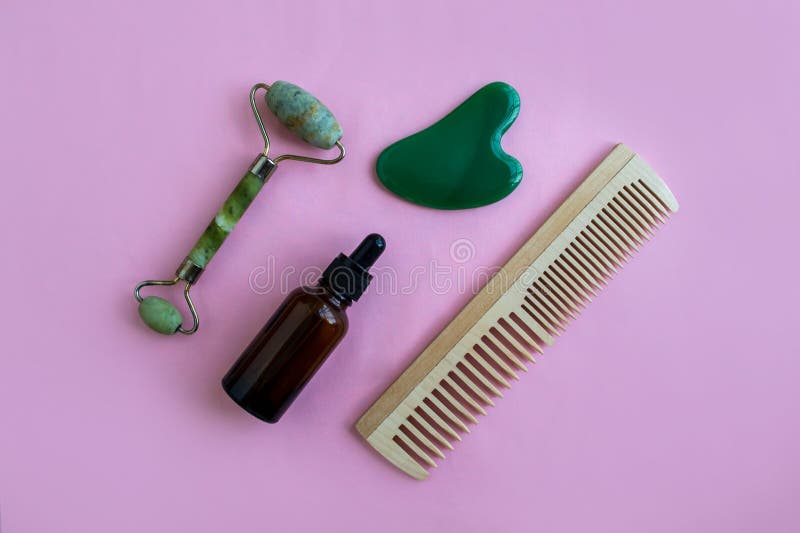 Jade massagers, comb and bottle for cosmetics on a pink background. Background with copy space royalty free stock images