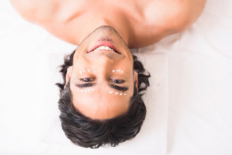 Happy young man is caring of his skin. He is lying with cream dots around his eyes and smiling. Happy young man is caring of his skin. He is lying with cream dots around his eyes and smiling