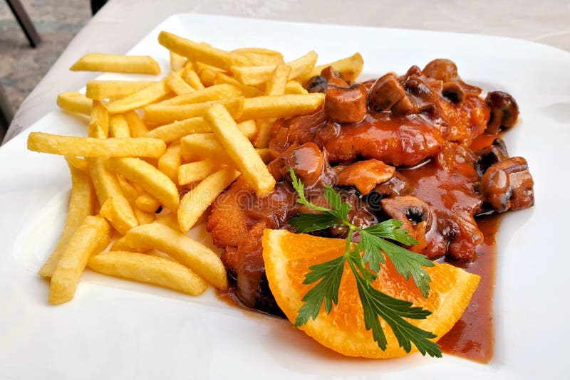 Jagerschnitzel alemán con una salsa y las patatas fritas, cierre de la seta para arriba en una placa blanca fotografía de archivo Jagerschnitzel alemán con una salsa y las patatas fritas, cierre de la seta para arriba en una placa blanca fotografía de archivo