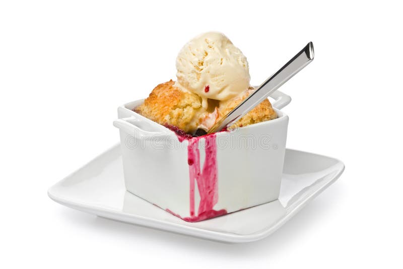 Individual size mixed berry cobbler with a scoop of vanilla ice cream and a spoon on a small plate against a white background. Individual size mixed berry cobbler with a scoop of vanilla ice cream and a spoon on a small plate against a white background.