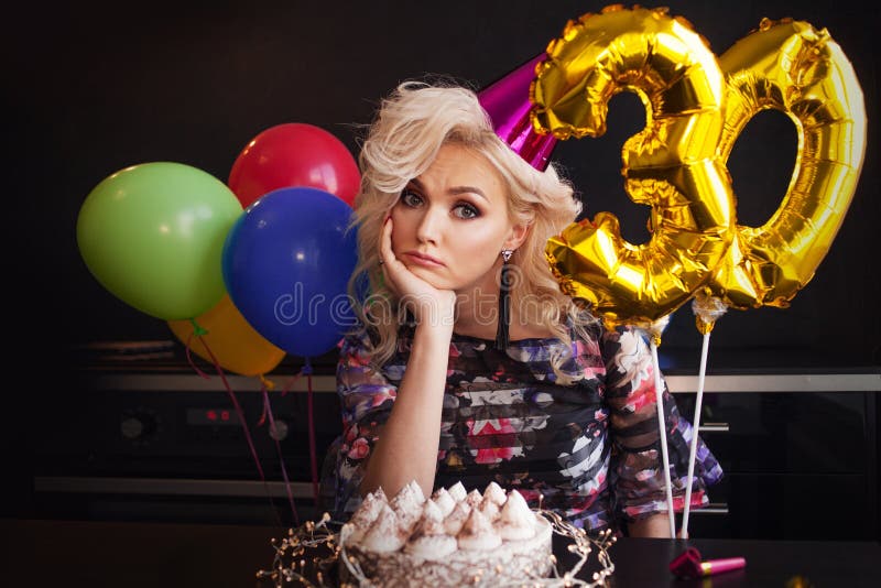 Jahrestagsgeburtstag Junge sch?ne Blondine sitzend vor einem Geburtstagskuchen und traurig lizenzfreies stockbild Jahrestagsgeburtstag Junge sch?ne Blondine sitzend vor einem Geburtstagskuchen und traurig lizenzfreies stockbild