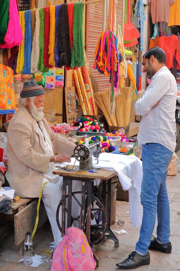 JAISALMER, RAJASTHÁN, LA INDIA - 19 DE DICIEMBRE DE 2017: Un hombre del sastre que trabaja en su máquina de coser fuera de su tie imagen de archivo JAISALMER, RAJASTHÁN, LA INDIA - 19 DE DICIEMBRE DE 2017: Un hombre del sastre que trabaja en su máquina de coser fuera de su tie imagen de archivo