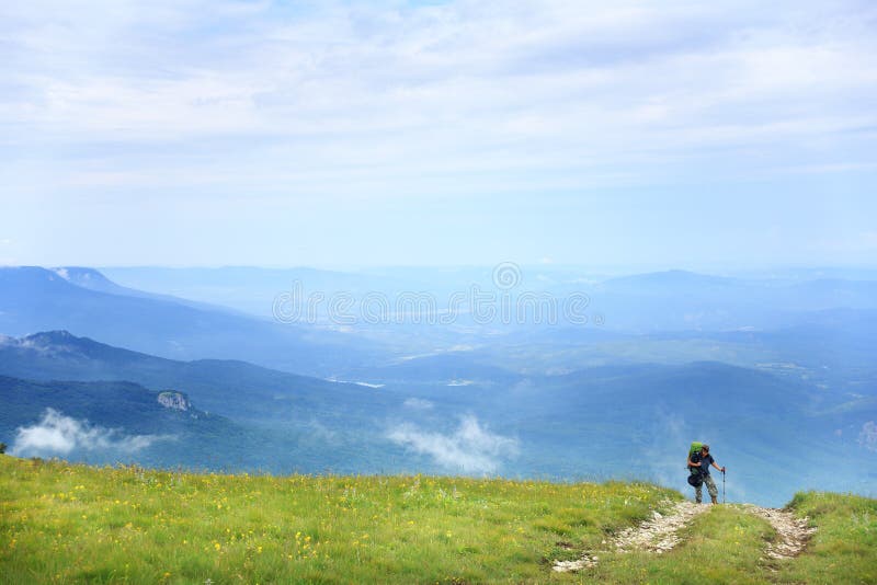 Jak długo przebić. Młoda kobieta chodzi na ścieżce w górę wzgórza z zieloną trawą na tle piękna halna sceneria pod błękitnym lata niebem z cloudscape z trekking słupami i plecakiem