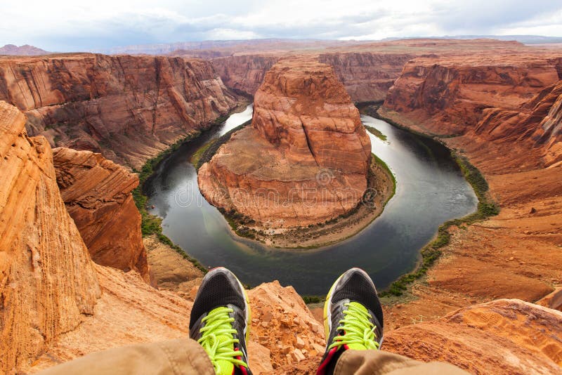Jambes d'homme de voyageur se reposant sur le fond de la courbure en fer à cheval de canyon, Arizona, Etats-Unis Concept de voyag photographie stock Jambes d'homme de voyageur se reposant sur le fond de la courbure en fer à cheval de canyon, Arizona, Etats-Unis Concept de voyag photographie stock