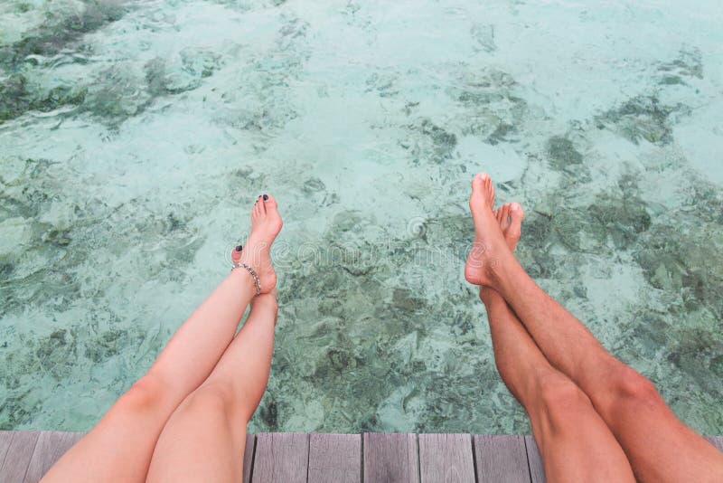 Jambes d'homme et de femme posées sur un pilier au-dessus de l'eau bleue claire images libres de droits Jambes d'homme et de femme posées sur un pilier au-dessus de l'eau bleue claire images libres de droits