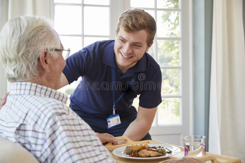 Jantar masculino do serviço do trabalhador do cuidado a um homem superior em sua casa