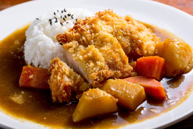 Japanese curry with rice, black sesame, carrot, potato and deep fries chicken in white dish on wooden table