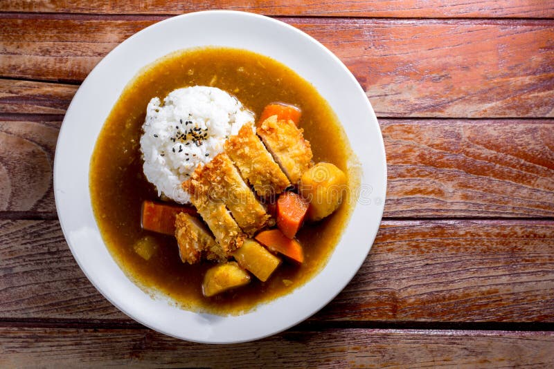 Japanese curry with rice, black sesame, carrot, potato and deep fries chicken in white dish on wooden table