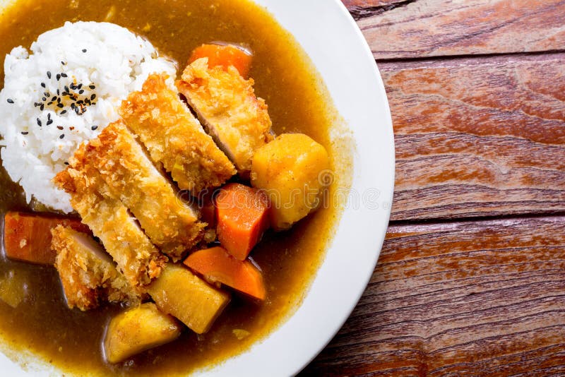 Japanese curry with rice, black sesame, carrot, potato and deep fries chicken in white dish on wooden table