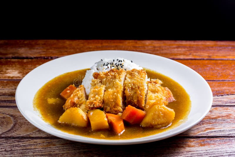 Japanese curry with rice, black sesame, carrot, potato and deep fries chicken in white dish on wooden table