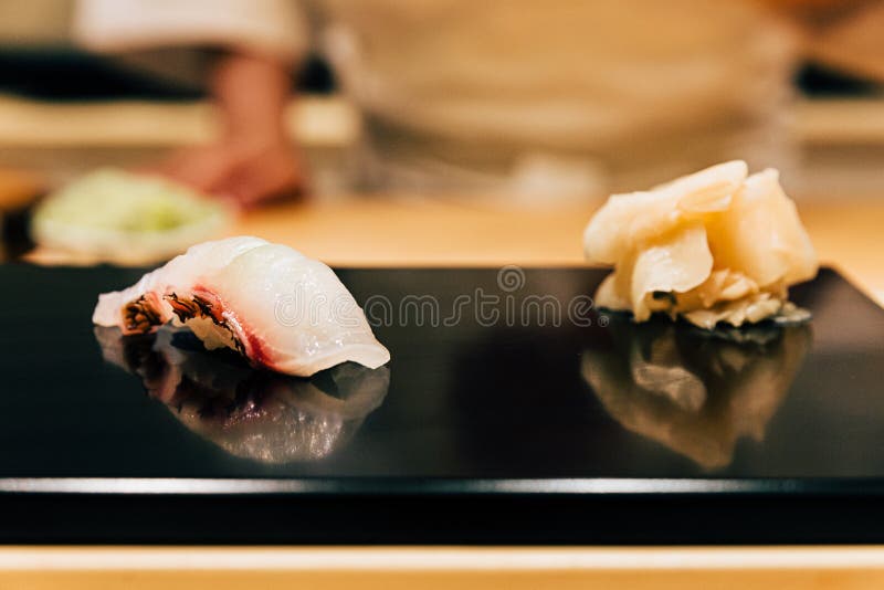 Japanese Omakase meal: Close up Tai Sea Bream fish Sushi served on glossy black plate with pickled ginger. Japanese luxury meal