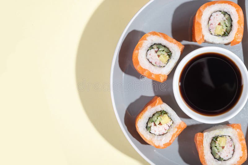 Japanese sushi with salmon, dragon rolls on a bright yellow background. Pop art. Tasty snacks on a gray plate and chopsticks. Asian traditional food