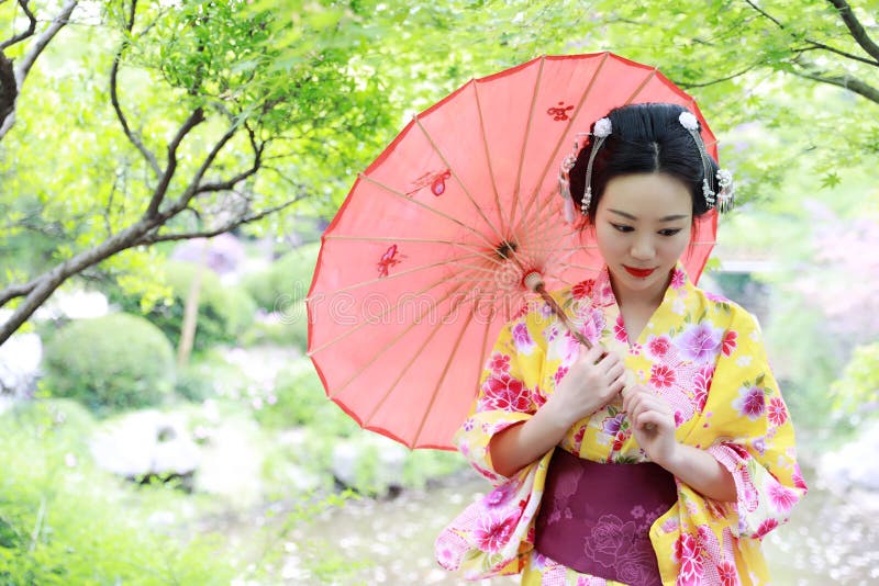 Traditional Asian Japanese beautiful Geisha woman wears kimono bride with a red umbrella in a graden