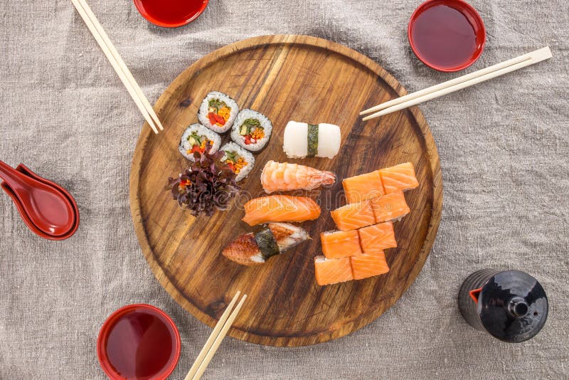 Japanischer Nahrungsmittelrestaurantsushi maki Rollensatz auf hölzernem rundem Brett mit Essstäbchen auf grauem Hintergrund des G lizenzfreie stockfotografie Japanischer Nahrungsmittelrestaurantsushi maki Rollensatz auf hölzernem rundem Brett mit Essstäbchen auf grauem Hintergrund des G lizenzfreie stockfotografie