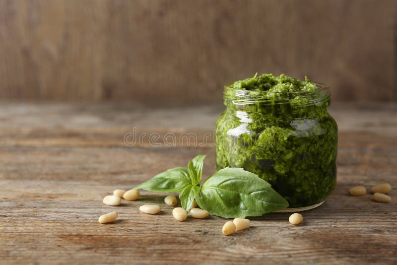 Jar of Pesto Sauce with Basil Leaves and Pine Nuts on Wooden Table