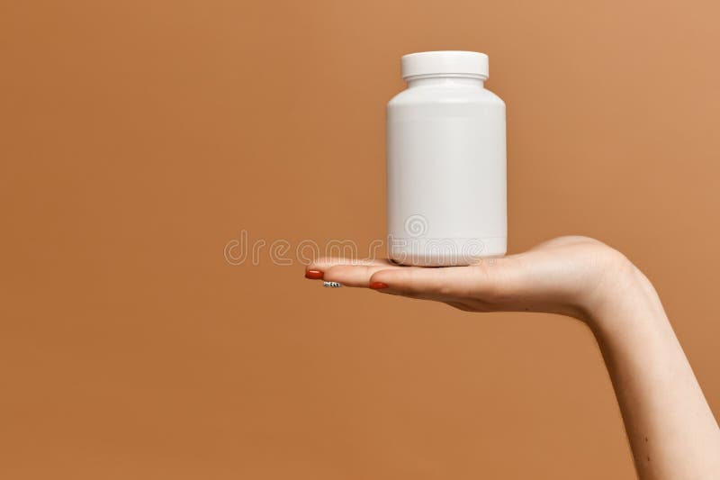 Jar with pills on the palm of the beautiful female hand  at the beige background. Jar with vitamins on tidy female hand, copy space. Improve immune in seasonal illness time. Concept of anti-flu and anti-viruses medicine