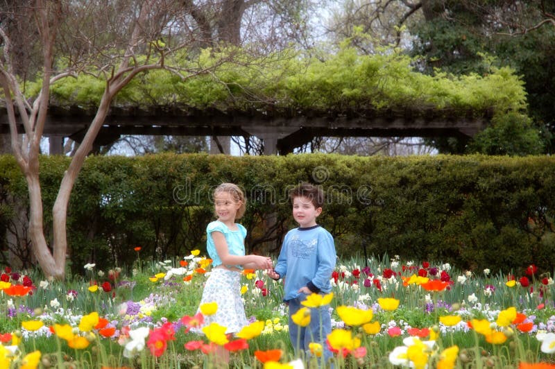 Two young friends a boy and a girl stand amongst blooming flowers in a beautiful garden. Two young friends a boy and a girl stand amongst blooming flowers in a beautiful garden.
